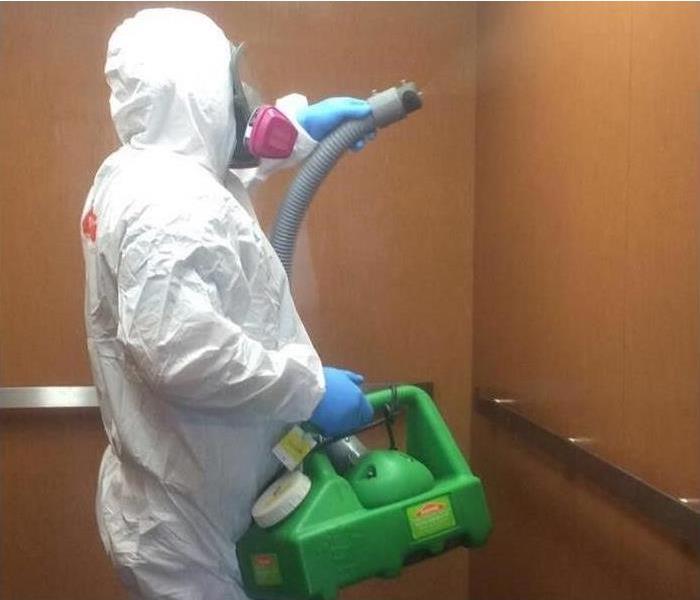 a person in full hazmat suit PPE with a servpro fogging machine cleaning a COVID-19 positive office space
