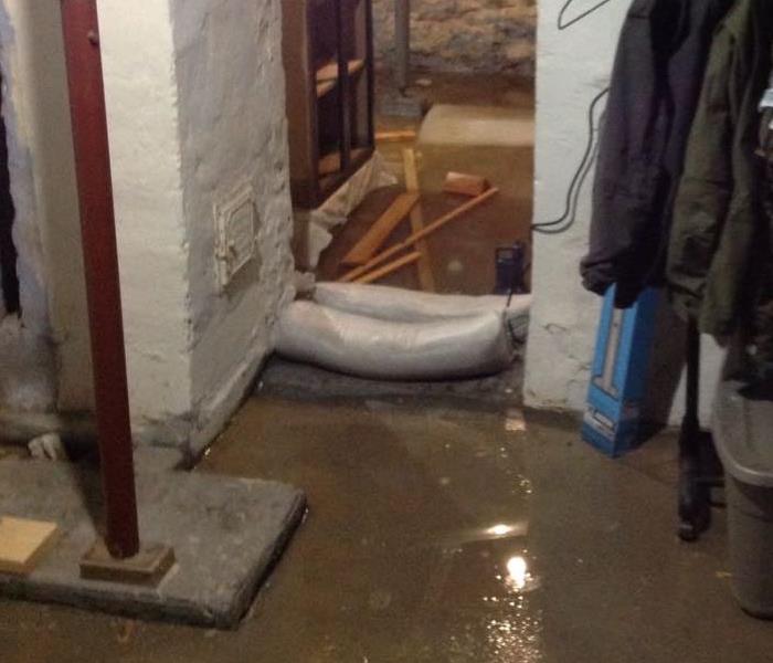 A Concrete basement with water standing and sand bags in place 