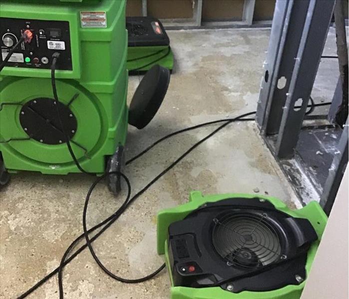 concrete floors with green air movers and humidifier adjacent to a removed water heater that malfunctioned 