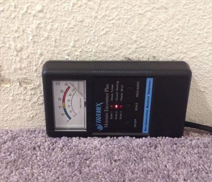 a hand holding a black moisture meter against a wet and saturated wall