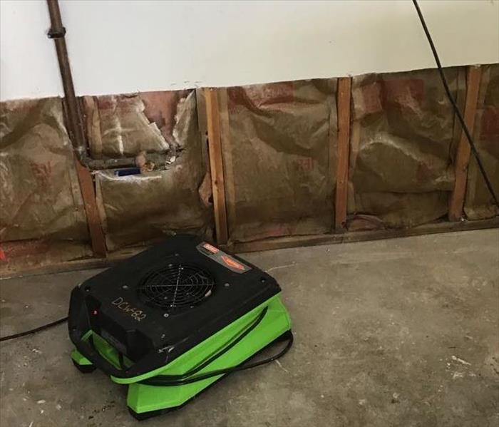 a basement after water damage with cement floor and a 2 foot dry flood cut and a green SERVPRO air mover 