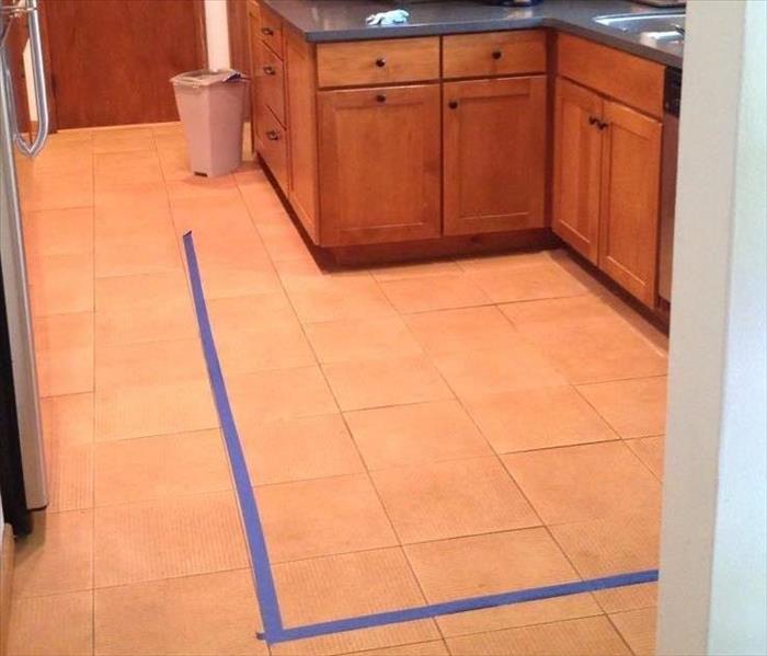 a kitchen with wood cabinets and flooring with a blue tape line is outlining the damaged flooring 