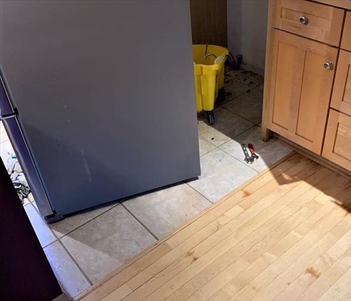 a kitchen with refrigerator moved into the open kitchen space to expose a broken water line  
