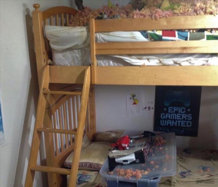 a room with bunk beds with roof insulation spread everywhere because of the tree that fell on the top bunk from a storm