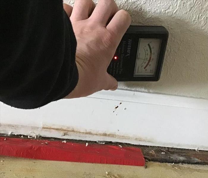 a man holding a moisture meter to the wall with moisture readings in the red