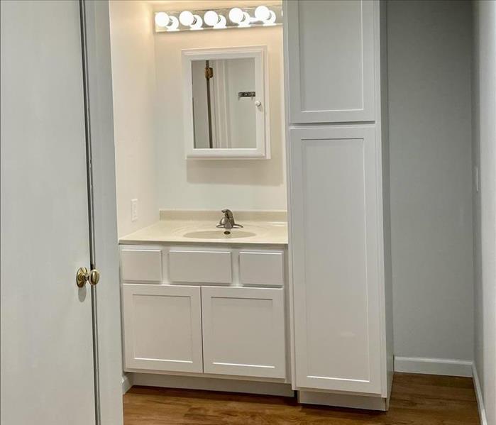 an apartment bathroom with white cabinets after being fully remodeled after a water loss 