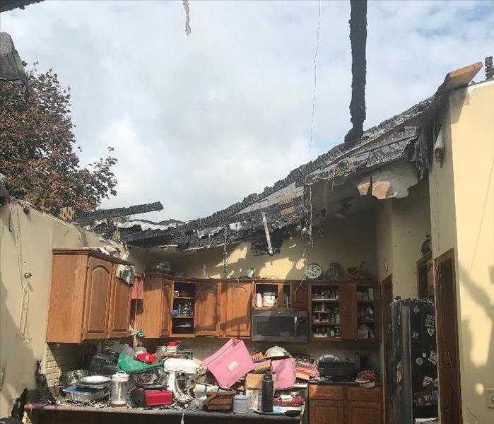a kitchen that has been severely damaged from a fire, the roof is exposed as the fire engulfed it, fire damage kitchen items 