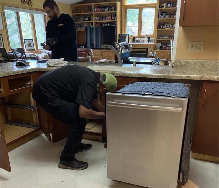two men in servpro ready uniforms working on a water loss in a kitchen from a broken dishwasher