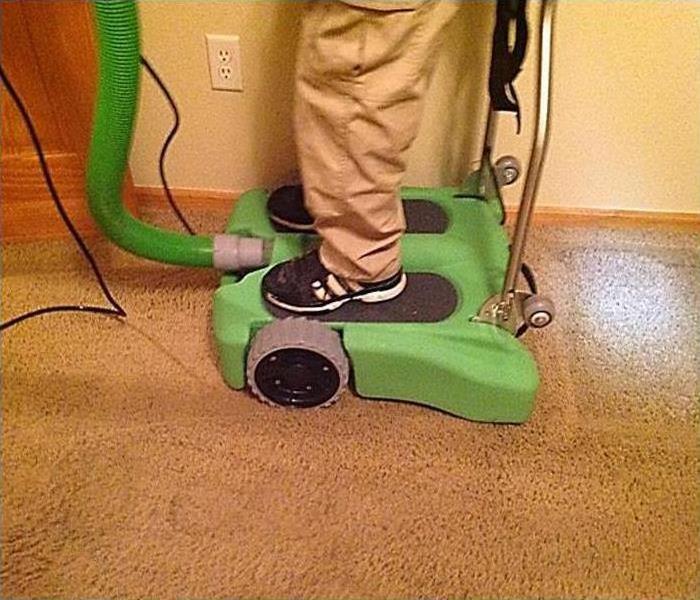 a man in khaki pants and a black polo using a servpro rover to extract water from flooded carpet