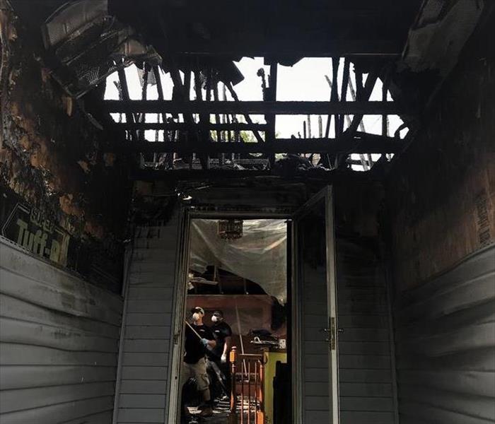 the entrance of a home that suffered extreme fire damage with the roof burnt off and two servpro technicians cleaning inside