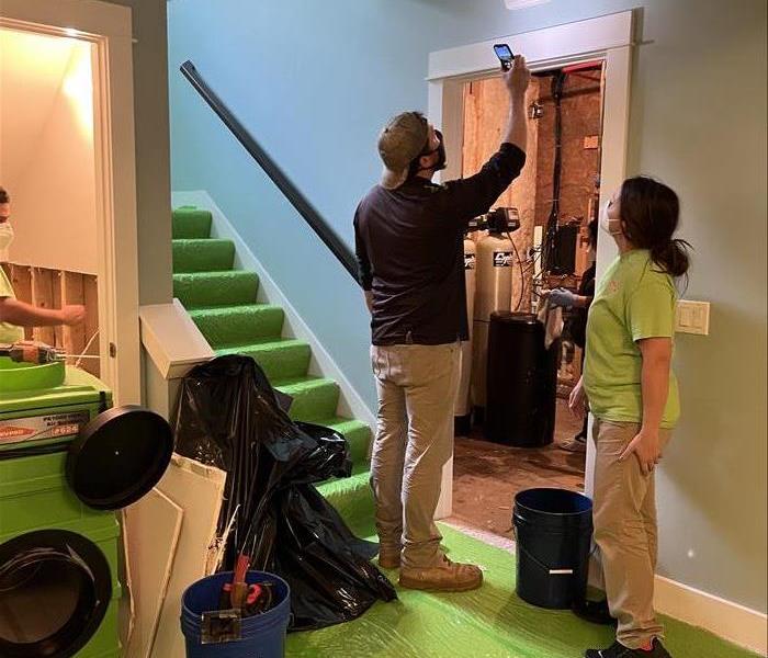 a man and woman in servpro uniform inspecting water damage in a basement 