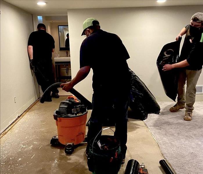 three male servpro technicians in servpro uniforms removing carpet in a finished basement that had storm damage