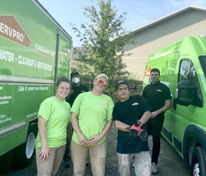 5 servpro crew members in servpro green and black uniforms standing next to 2 servpro green trucks