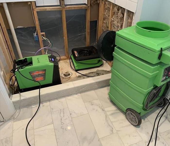a bathroom with green servpro drying equipment in place for water damage restoration 