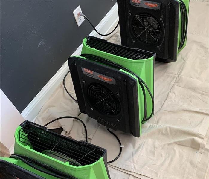three air fans lined up in a row in a family room that had water damage from frozen pipe break 