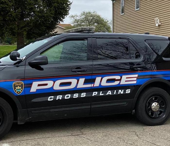 a blue cross plains squad car in front of a tan building 