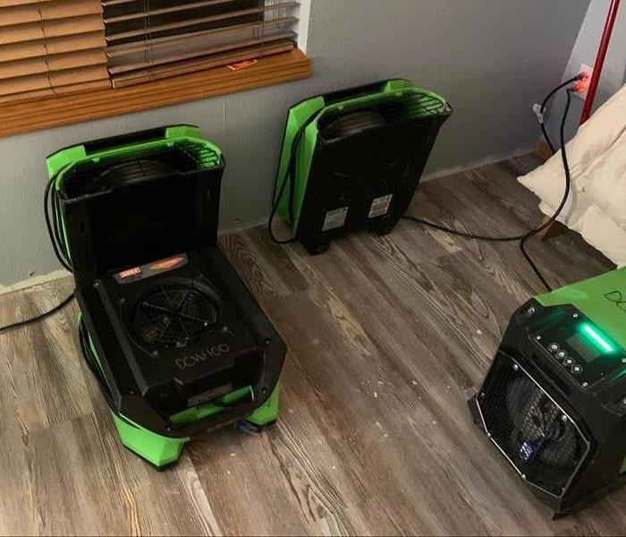 servpro air movers and dehumidifiers drying a room with gray walls and hardwood floors 