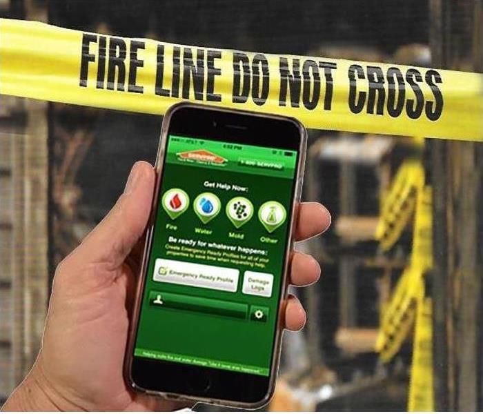 a hand holding a smart phone with SERVPRO ERP app with background of fire damage 